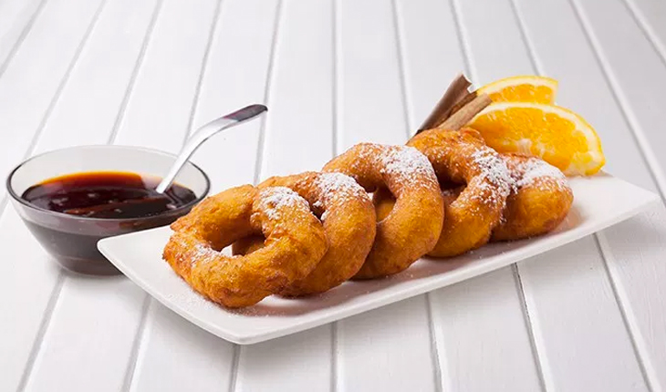 A plate of several picarones. Doughnut like pastries with powered sugar on top.
