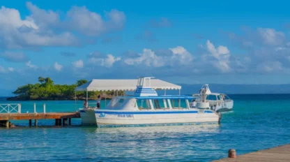Two boats are docked at a wooden pier on clear blue water, perfect for a school travel program adventure, with a small island and a cloudy sky visible in the background.
