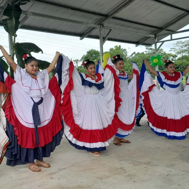 Four women perform a traditional dance in colorful, layered dresses under a canopy.