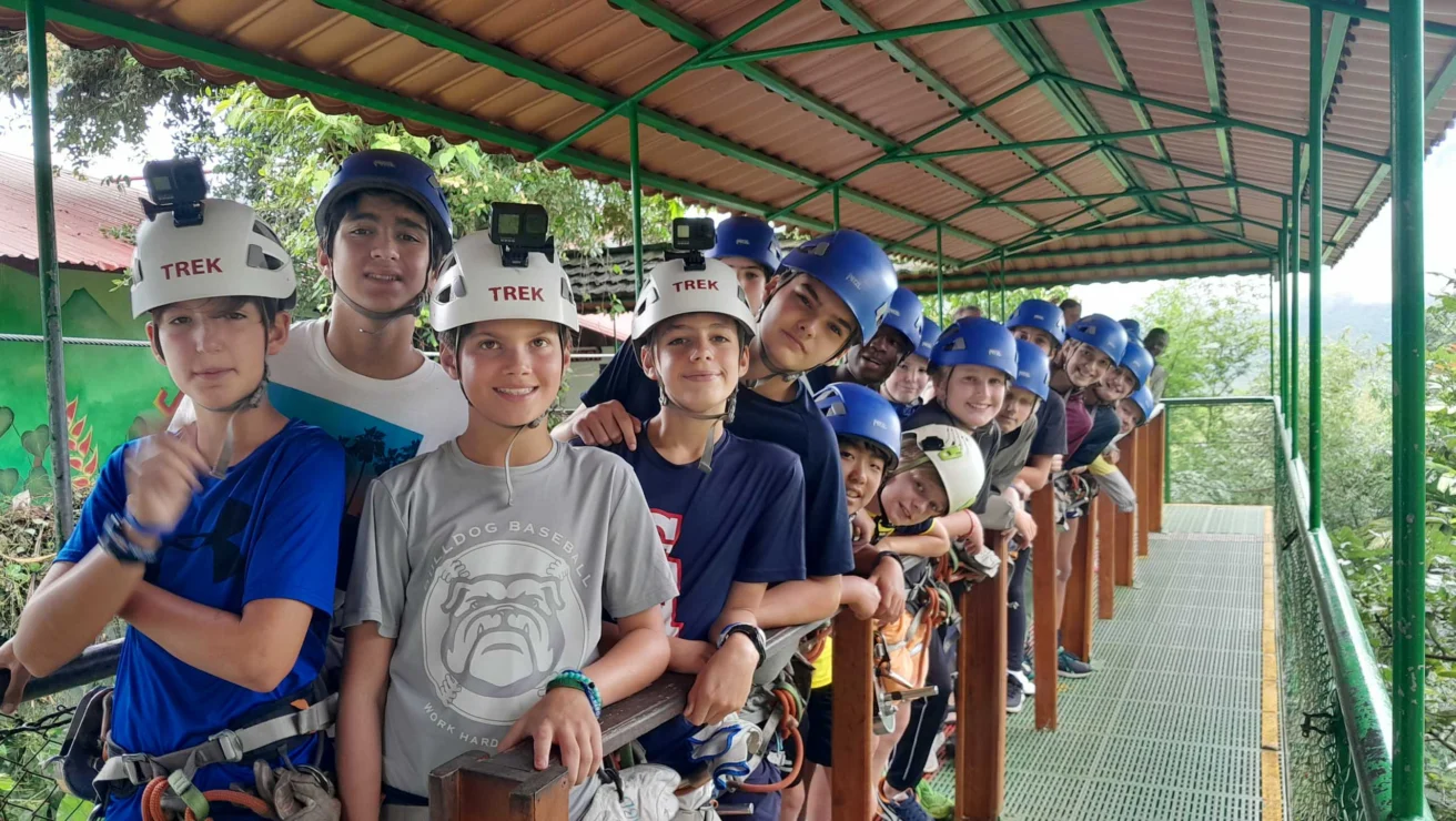 A group of people wearing helmets and harnesses stands on a platform, preparing for an outdoor adventure activity.