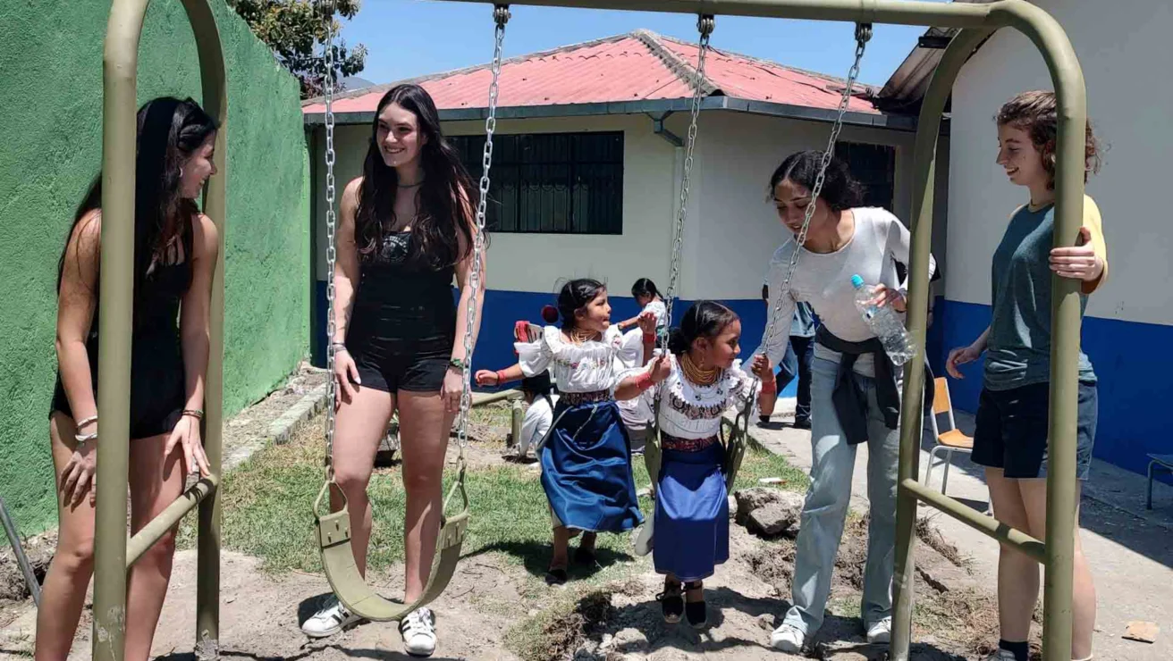 A group of students playing with children on a swing.