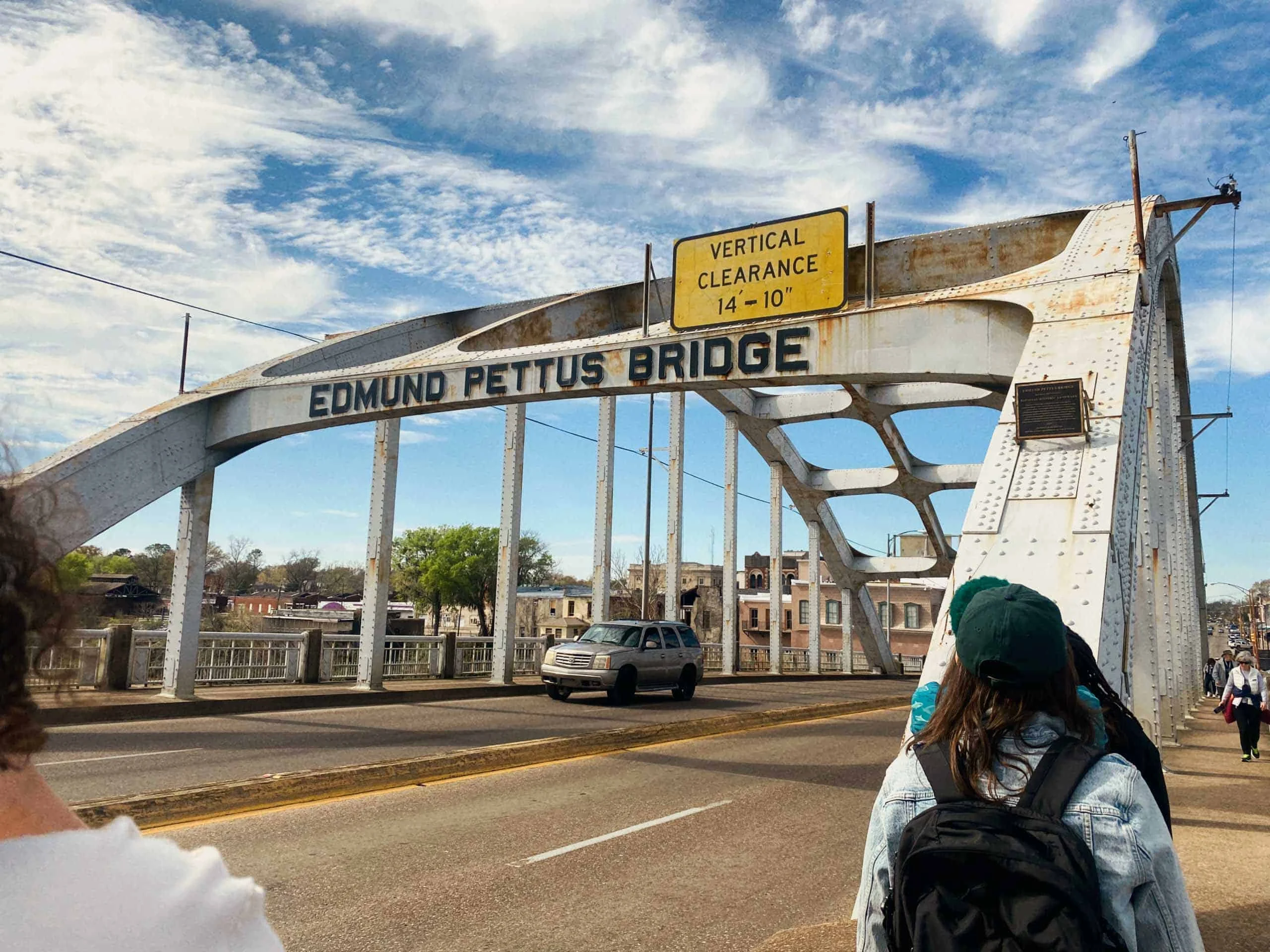 Students walk across the Edmund Pettus Bridge in Selma, Alabama on a partly cloudy day, with a car driving beside them—an inspiring scene for a civil rights school trip.