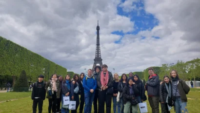 A group of people stands on grass with the Eiffel Tower in the background. The sky is cloudy.