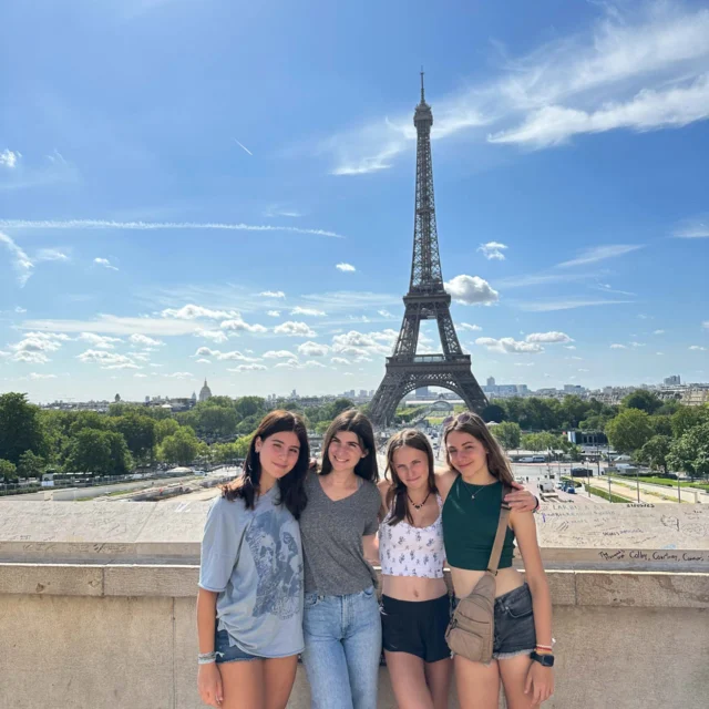 Four people standing together in front of the Eiffel Tower on a sunny day.