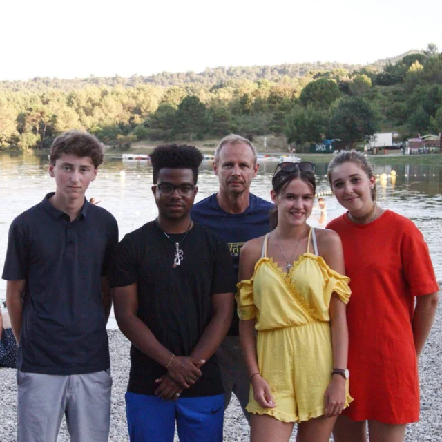 Five people standing together outdoors near a lake with trees in the background.