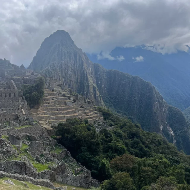 View of Machu Picchu with terraced ruins and a mountain backdrop under a cloudy sky.