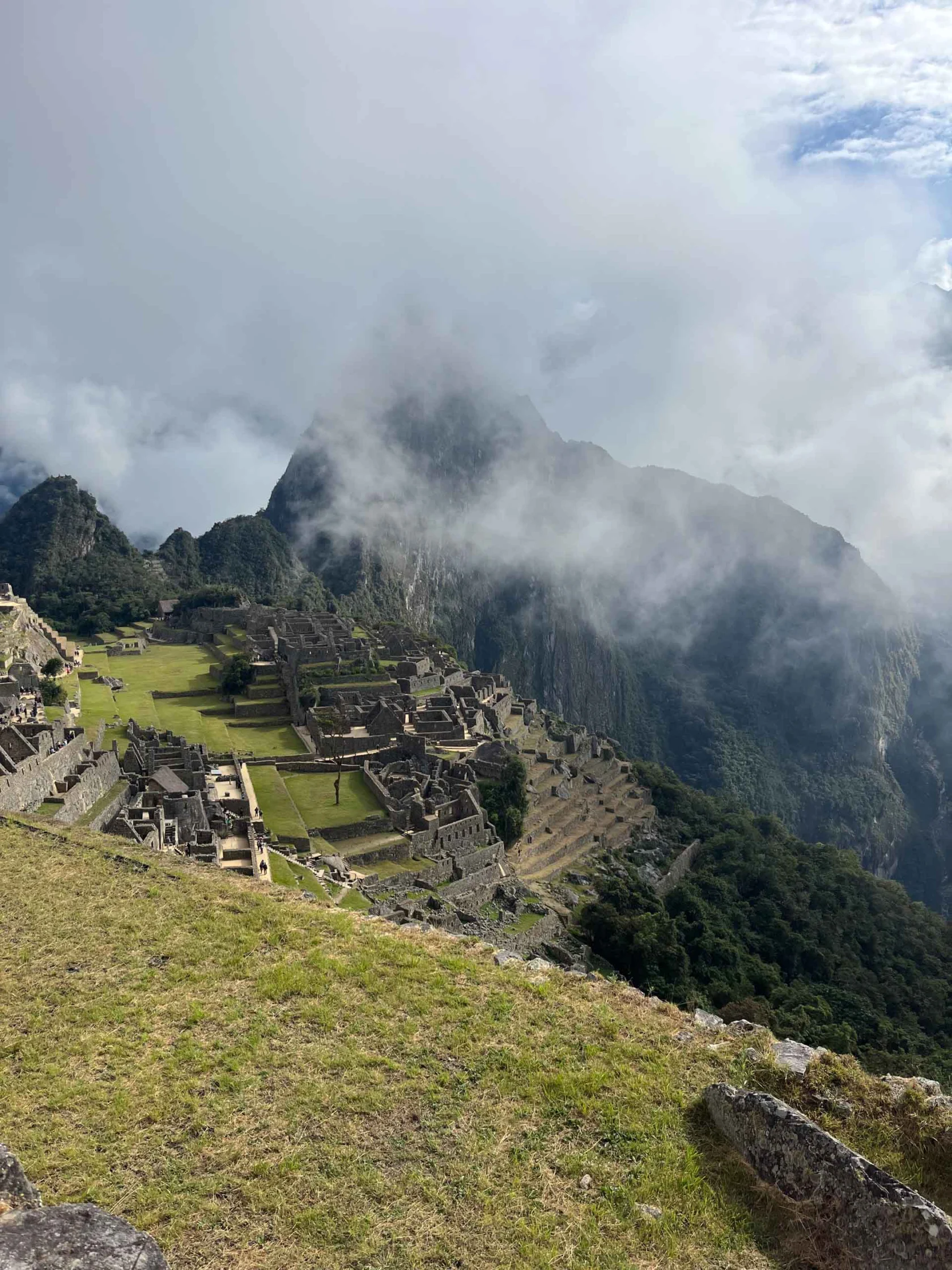 View of Machu Picchu with ancient stone structures on a hillside and misty mountains in the background.