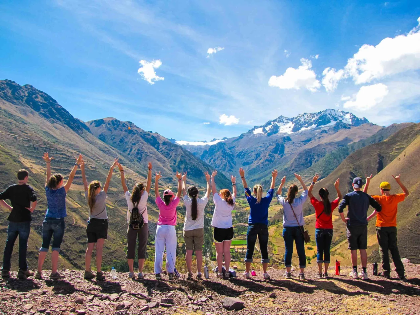 A group of teens raise their arms on a ridge above the mountains of Peru's Sacred Valley.
