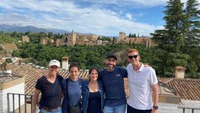 A group of five people standing together with a scenic view of a historic city and green landscape in the background.