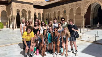 A group of people posing in a sunny courtyard with intricate architectural details.