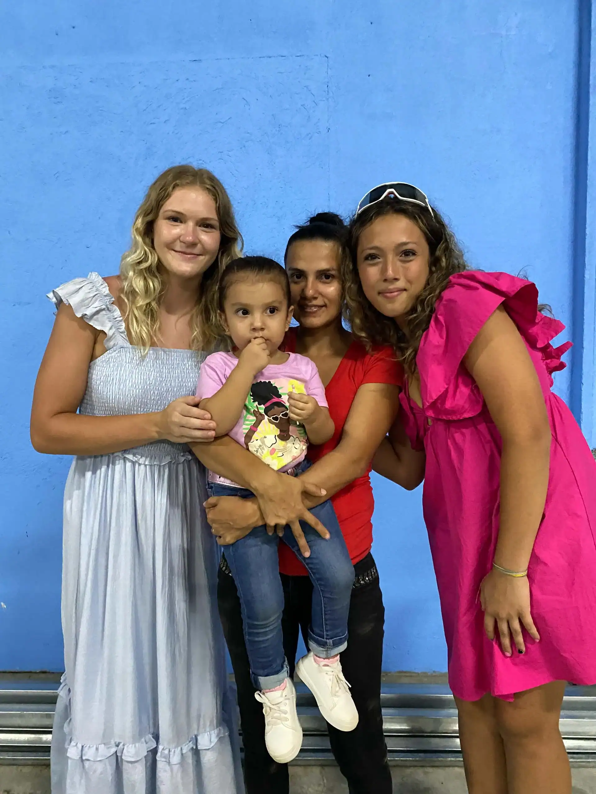 Four people pose in front of a blue wall; an adult holds a young child, with two others—perhaps sharing stories of student travel to Costa Rica—standing on either side, all looking at the camera.