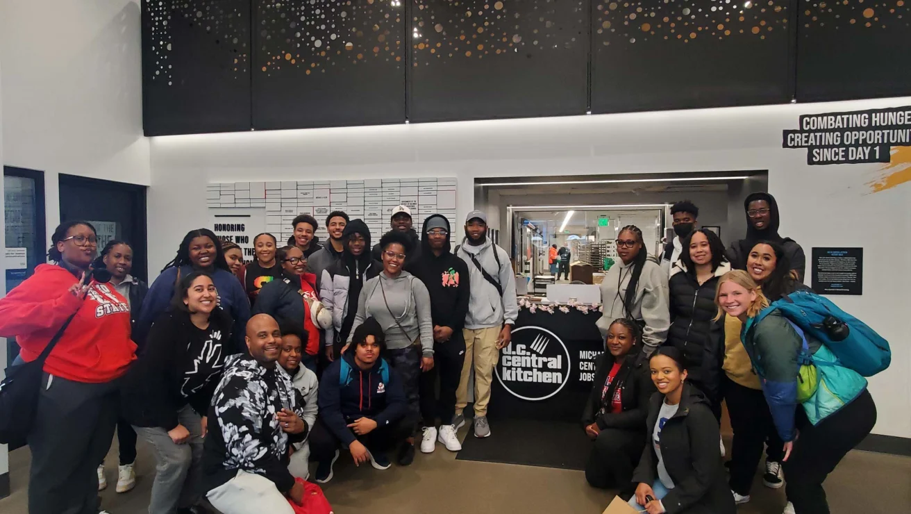 A group of people pose for a photo in front of a Central Kitchen sign inside a building.