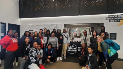 A group of people pose for a photo in front of a Central Kitchen sign inside a building.