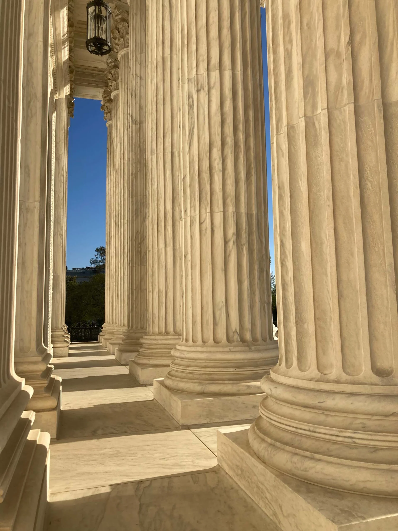 Tall marble columns with intricate capitals line a hallway, casting long shadows on the floor.
