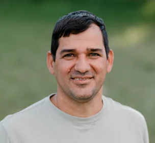 A man with short dark hair stands outdoors wearing a gray t-shirt with "A. EAGLE USA" on the front, smiling at the camera.