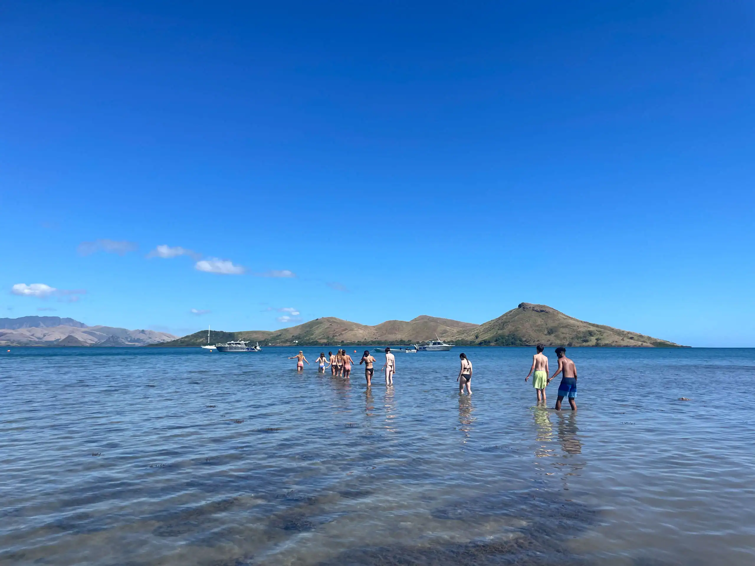 People on a conservation trip walking in shallow water toward an island under a clear blue sky.