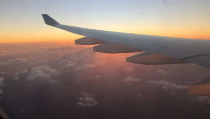 View from an airplane window showing the wing against a vibrant sunset sky with clouds below.