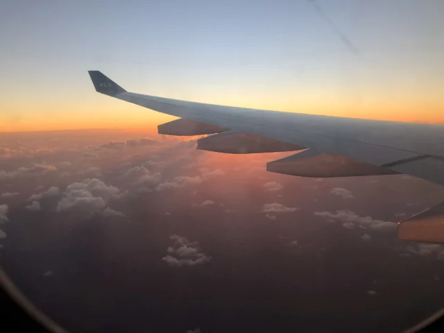 View from an airplane window showing the wing against a vibrant sunset sky with clouds below.