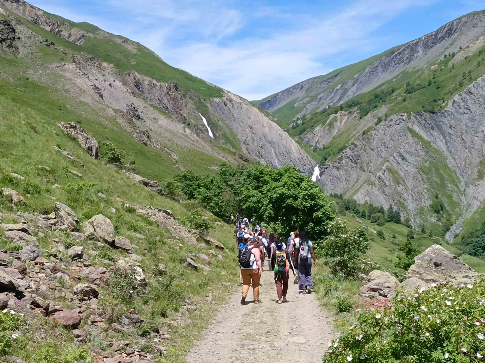 A group of people hiking on a dirt path through a mountainous landscape under a clear blue sky.