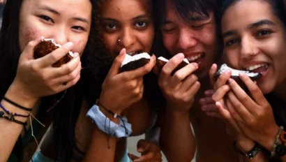 A group of five people at the beach eating snacks and smiling.