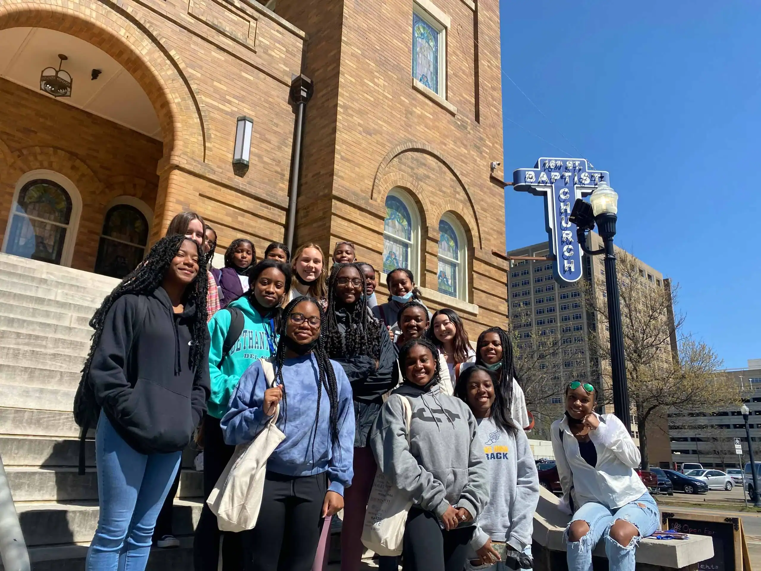 A group of teenagers poses for a photo on the steps outside a brick building with a sign reading "16th St Baptist Church," capturing an unforgettable moment during their american history travel experience.