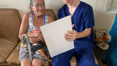 A young student on a medical study abroad school trip in Costa Rica in blue scrubs reviews a document with an older woman in a clinic setting.