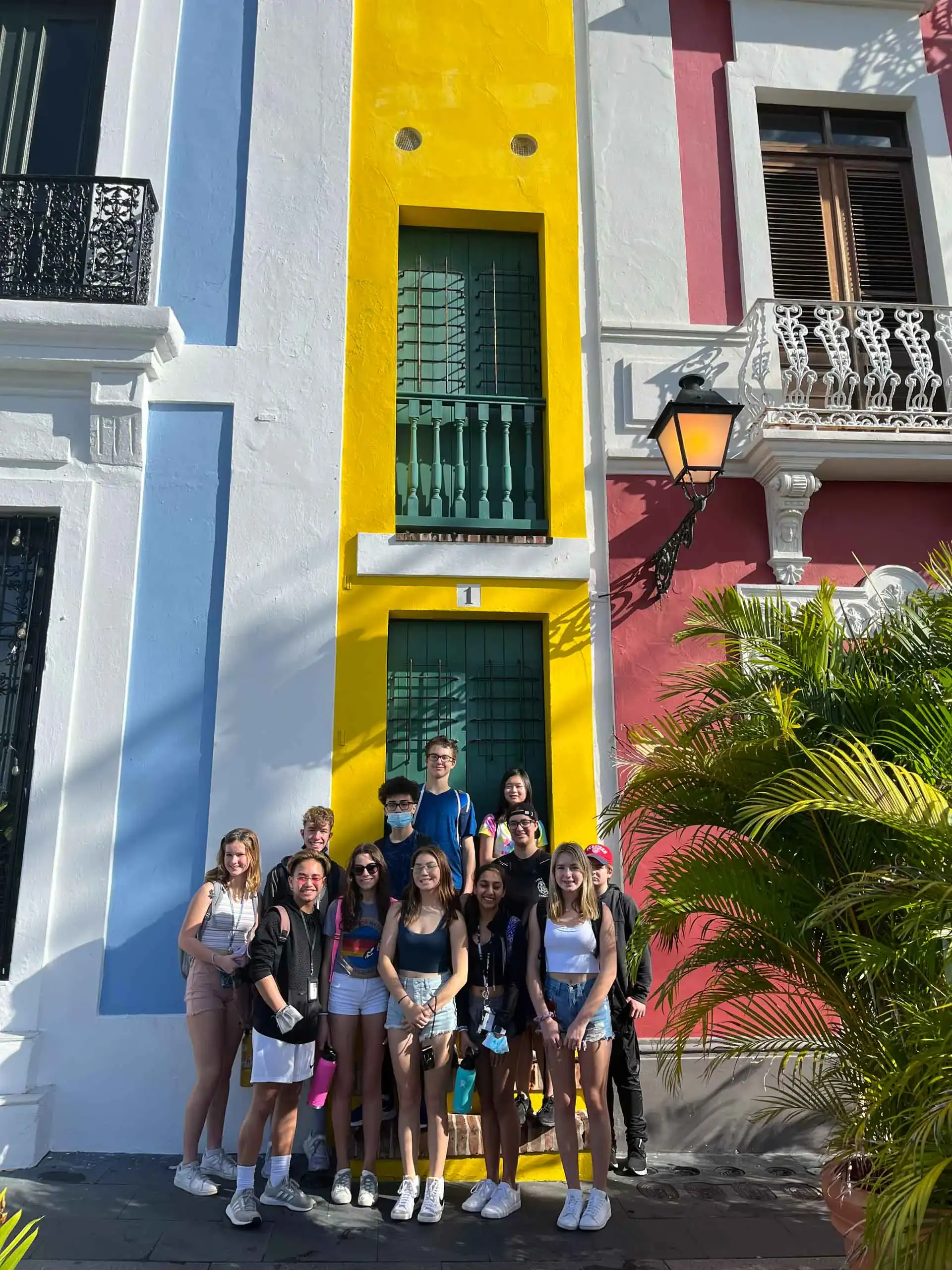 A group of student travelers posing for a photo in front of a colorful building during their school trip to Puerto Rico.