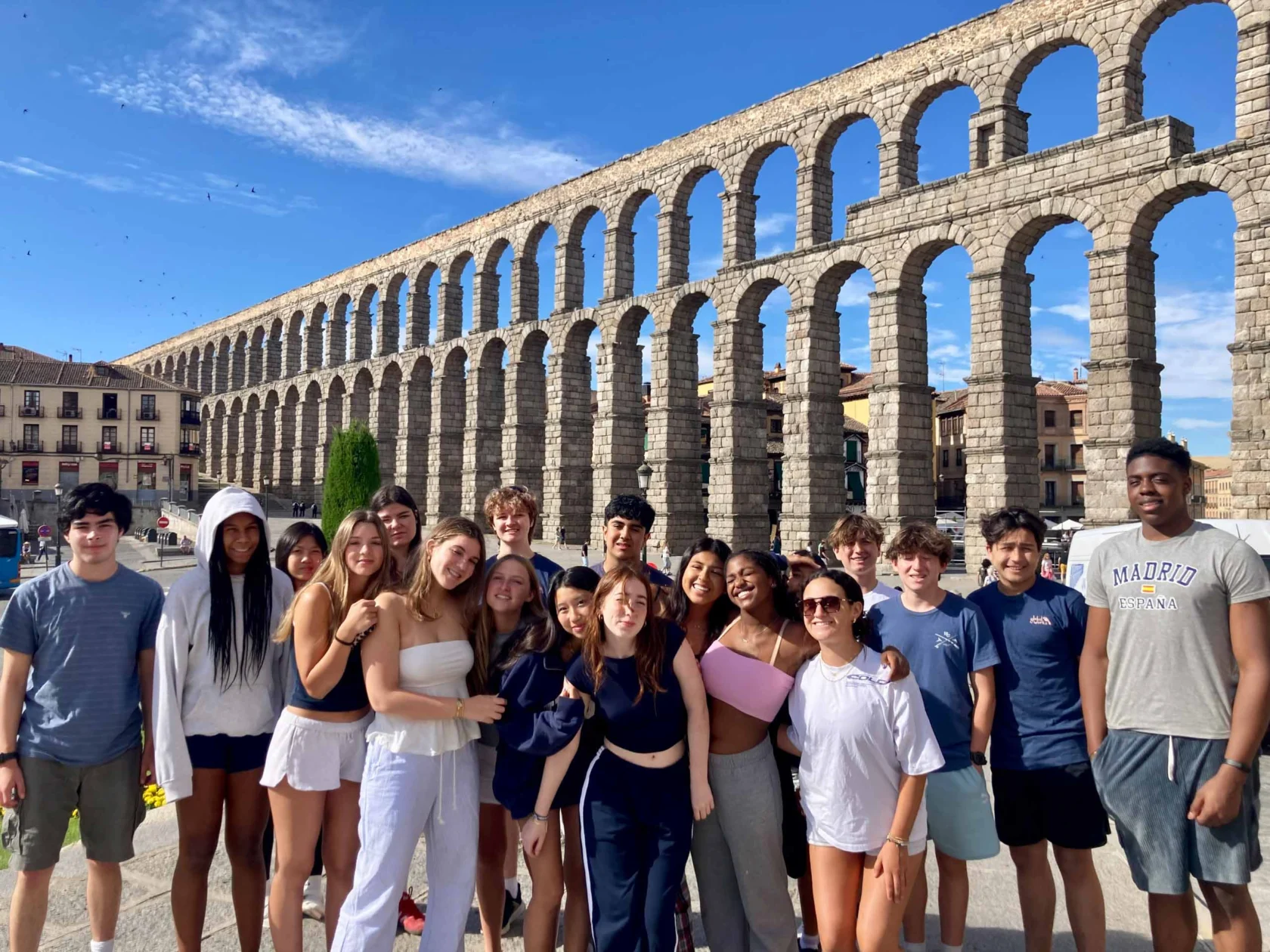A group of people posing in front of an ancient stone aqueduct under a clear blue sky.