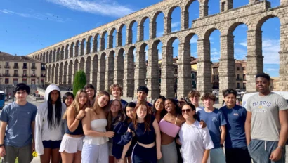 A group of people posing in front of an ancient stone aqueduct under a clear blue sky.