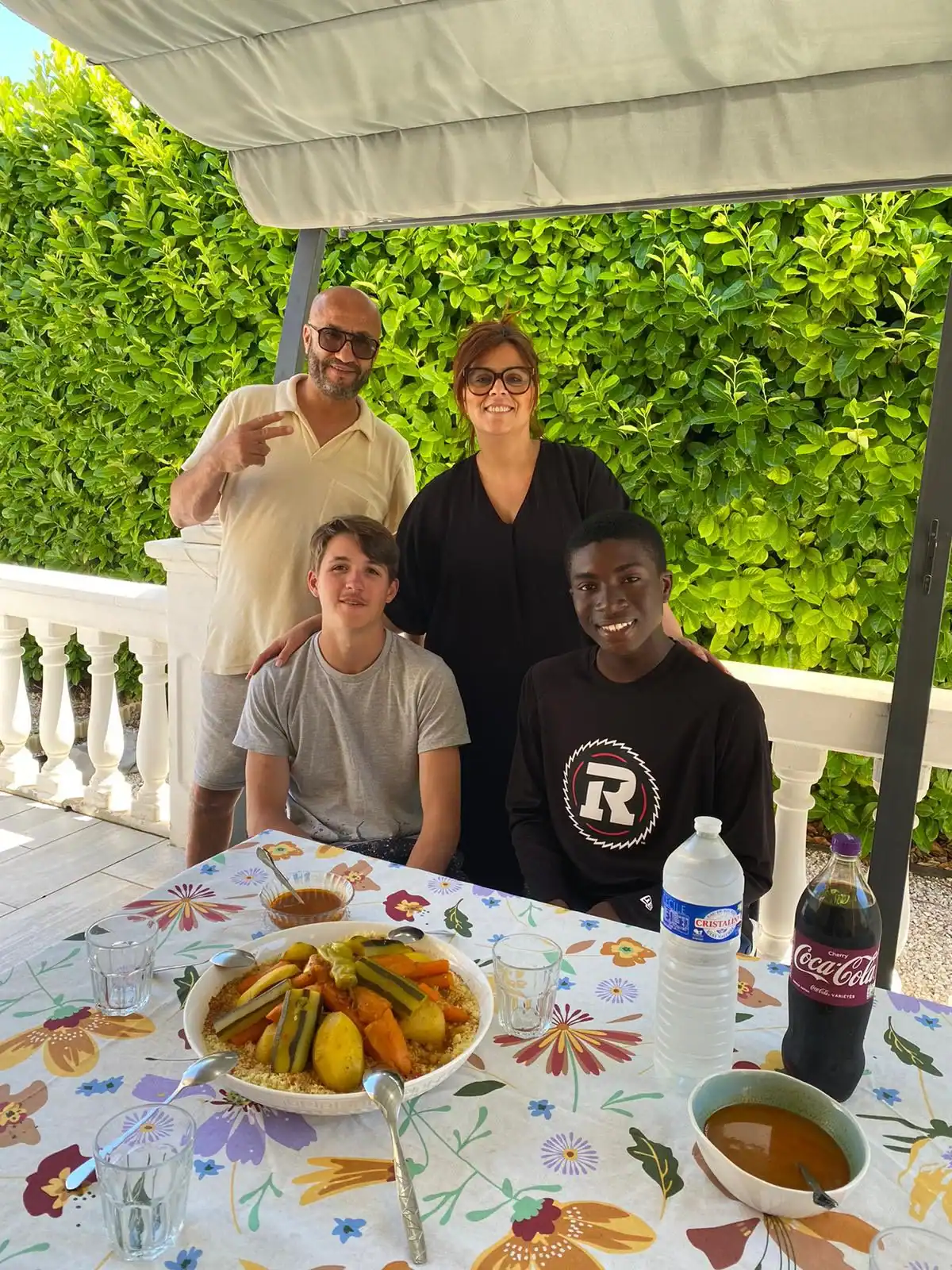 Four people pose and smile by a table set with food, drinks, and plates on a covered patio with greenery in the background during their language immersion trip.