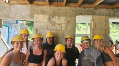A group of eight people wearing yellow hard hats and casual work clothes stand together in a partially constructed building.