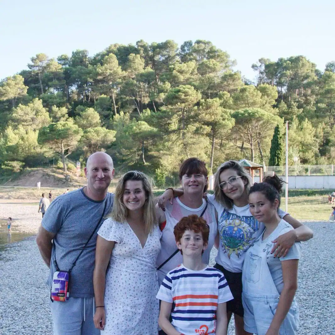 Six people pose together on a rocky beach with trees and greenery in the background. It is daytime, and they are smiling at the camera during their student trip to France.