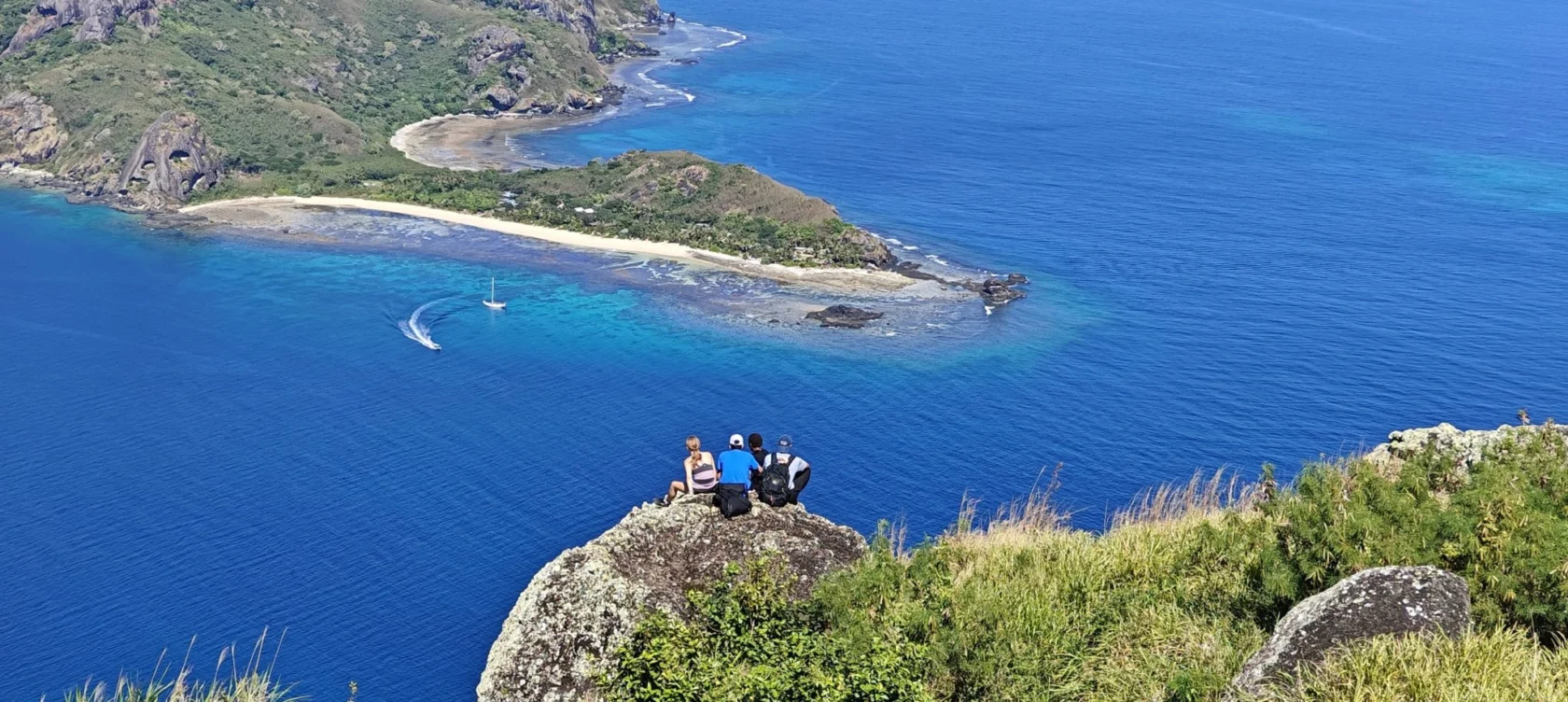 three people sitting on the ground overlooking the water.