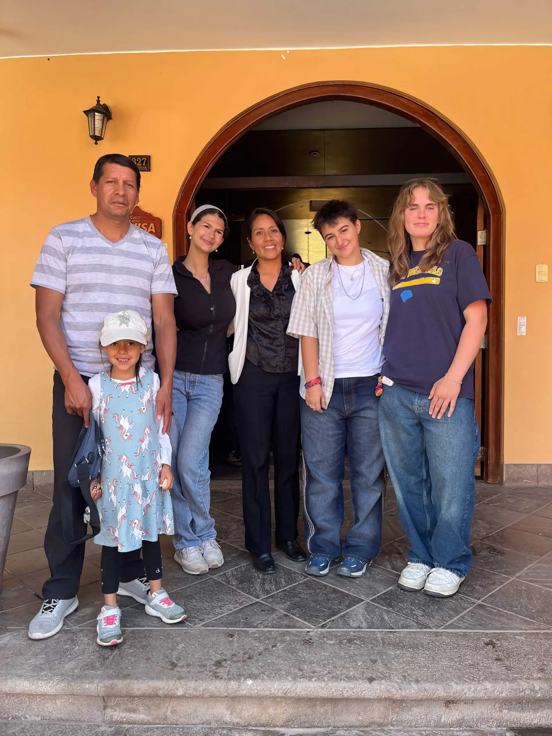 A group of six people on their student trip to Peru stand in front of an arched doorway. They are smiling and casually dressed.