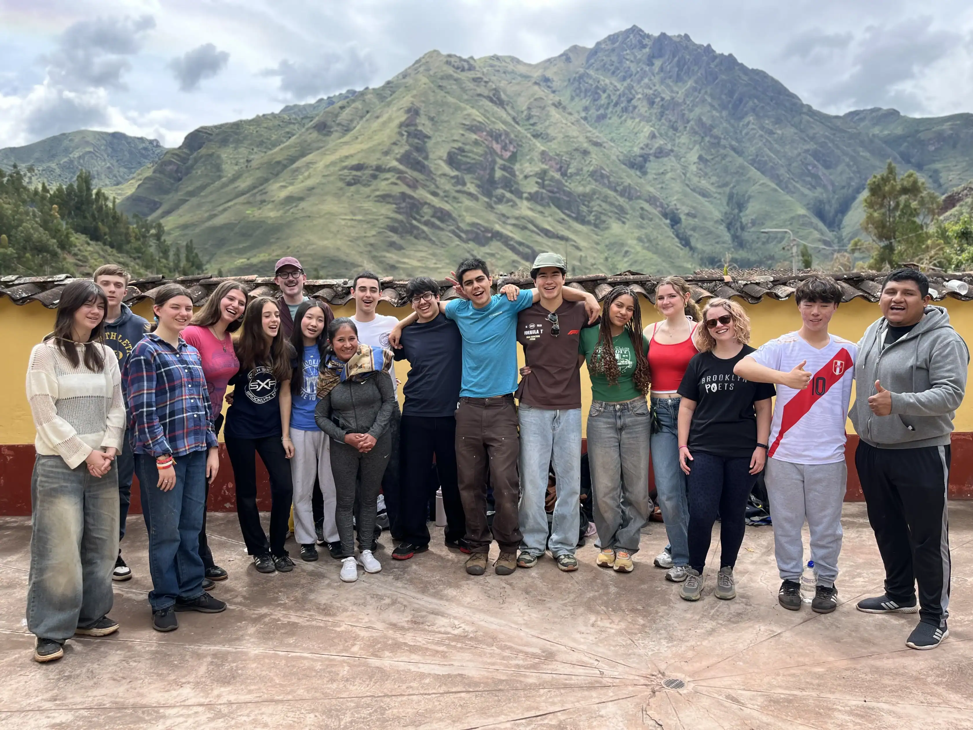 A school group travel adventure: a group of young adults poses together outside with green mountains in the background under a partly cloudy sky in Costa Rica.
