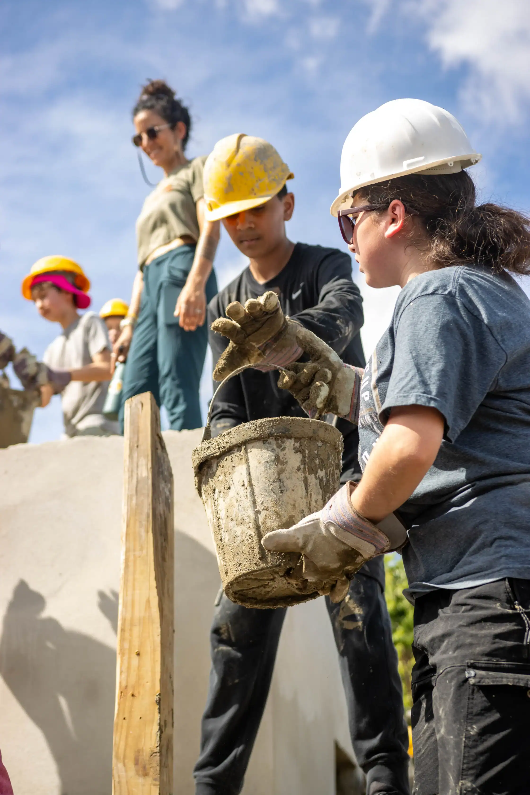 A group of people wearing hard hats working together to mix and carry wet cement.