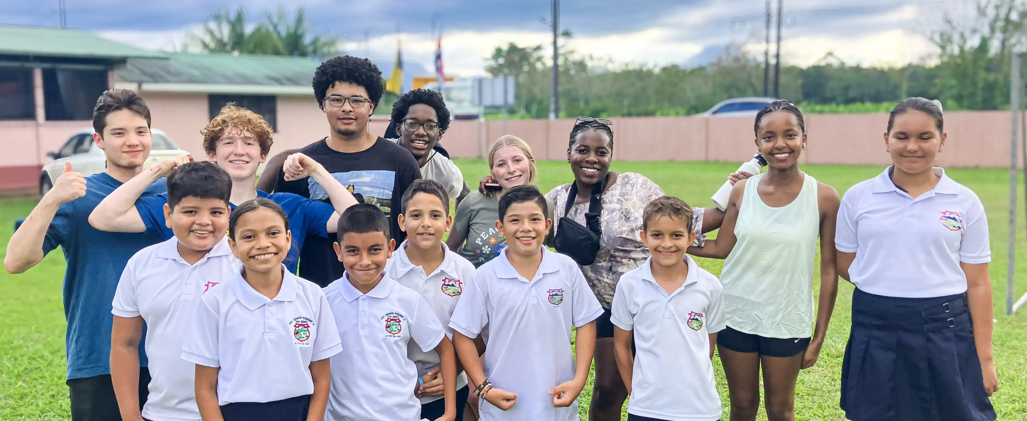 A group of students and teachers smiling and posing together on a grassy field.