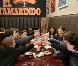A group of young people sit around a restaurant table at El Tamarindo, raising their glasses in a toast. Plates and napkins are set on the table.