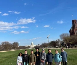 A group of eight children stand in a line on the National Mall in Washington, D.C., with the U.S. Capitol building visible in the background under a blue sky.