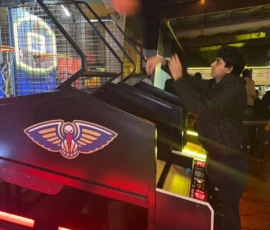A person plays an arcade basketball game indoors, aiming to shoot a ball into the hoop.