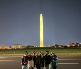 A group of eight people stand in front of the illuminated Washington Monument at night.
