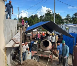 A group of people work together on a construction site, mixing and transporting concrete next to a cement mixer under a canopy.