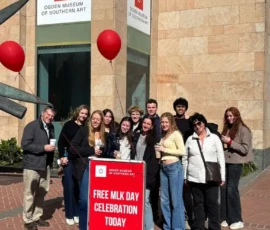A group of people stand outside the Ogden Museum of Southern Art with balloons and drinks near a sign that reads, "Free MLK Day Celebration Today.