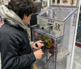 A person uses a penny press machine in a store, turning a crank to flatten a penny into a souvenir coin.