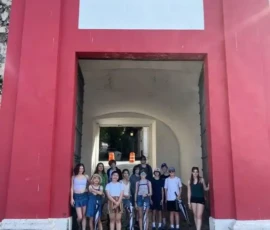 A group of people stands in front of a large red and white arched gate, posing for a photo on a sunny day.