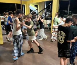 A group of children practice partner dancing indoors under bright lights, wearing casual and comfortable clothing.